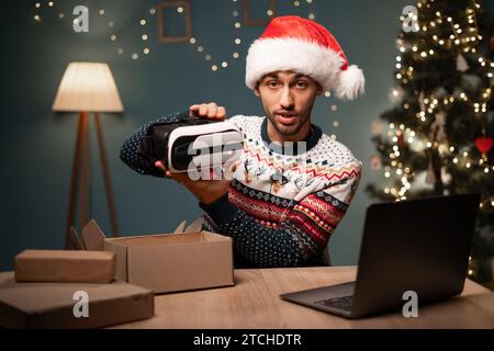 Vlogger maschio arabo nel pacchetto Babbo Natale con occhiali VR alla fotocamera, vista webcam. POV uomo musulmano che registra video per il blog tecnologico a casa. Tecnologia Foto Stock