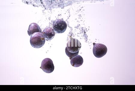 Fichi freschi che cadono nell'acqua isolati su sfondo bianco. Fotografia del cibo. Copia sfondo spazio Foto Stock