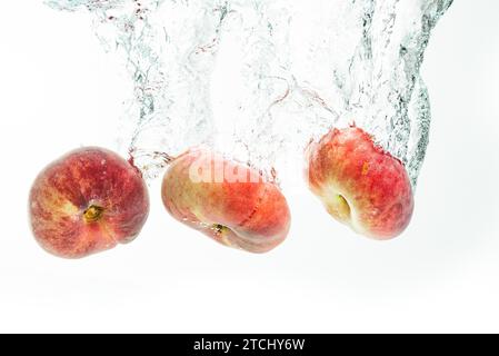 Mazzo di pesche ciambelle isolate su sfondo bianco, che spruzzano in acqua. Frutta che affonda in acqua cristallina con bolle d'aria Foto Stock