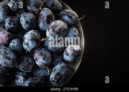 Prugne mature nel recipiente. Vista dall'alto su sfondo nero. Spazio copia a destra Foto Stock