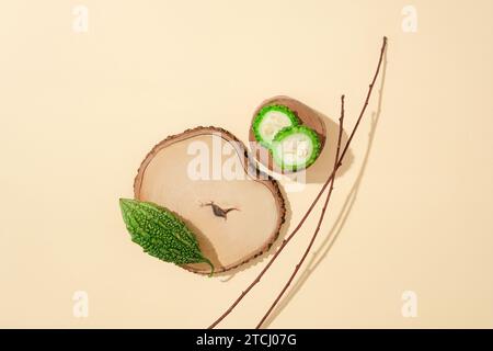 Due fette di melone amaro su una piattaforma di legno, un melone amaro su un tronco e rami secchi su uno sfondo pastello. Spazio di copia per la pubblicità dei prodotti Foto Stock