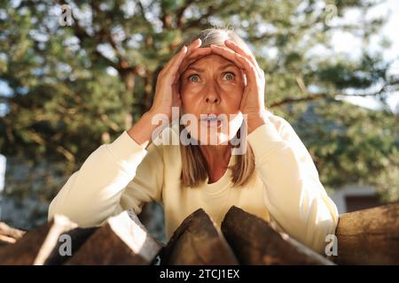 Concetto di vita privata. Curiosa donna anziana che spiava i vicini di casa sopra la legna da ardere all'aperto Foto Stock