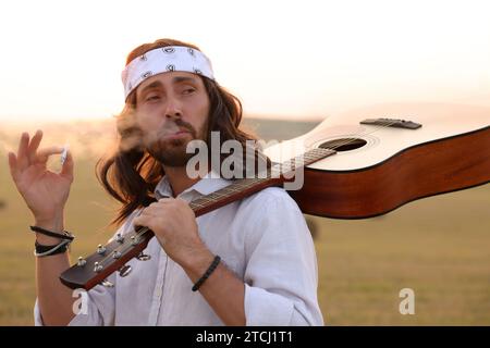 Elegante uomo hippie con fumante chitarra in campo Foto Stock