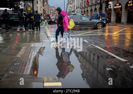 Gli acquirenti di Natale e altri pedoni negoziano una pozzanghera e attraversano Piccadilly in un pomeriggio piovoso a Westminster, il 12 dicembre 2023, a Londra, in Inghilterra. Foto Stock