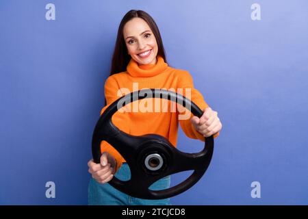 Foto di una giovane donna sorridente che impara a guidare per la prima volta girando lentamente il volante isolato su sfondo di colore viola Foto Stock