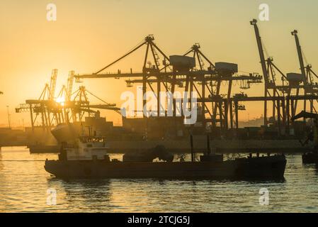 Una vista panoramica di un porto con grandi gru industriali che torreggiano su grandi barche Foto Stock