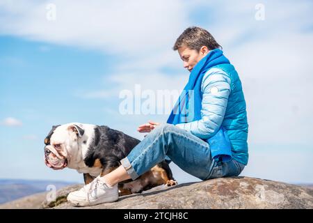 Una donna felice con i bulldog inglesi in cima alla montagna al Peak District nelle calde giornate di sole. Addestramento dei cani. Concetto di tempo libero Foto Stock