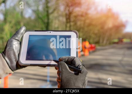 Tecnico del cantiere che utilizza il tablet con controller touch screen durante i lavori stradali. Crea utilizzando tablet con controller touch screen per controllare il posizionamento totale Foto Stock
