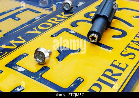 Primo piano della rimozione di un vecchio cartello auto giallo. Viti speciali e chiave Foto Stock