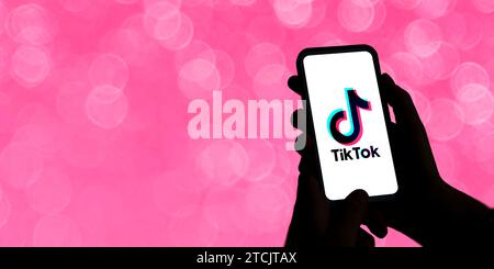 Donna che tiene un telefono cellulare con il logo TikTok sullo schermo. Intrattenimento breve video social network. Illustrazione con concetto adolescenziale. Contrasto elevato Foto Stock