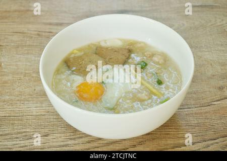 porridge di riso purè di maiale con cipolla primaverile tritata e tuorlo d'uovo tritato con prezzemolo sul recipiente Foto Stock