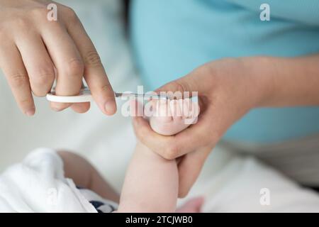 Le mani della mamma tagliano le unghie del neonato con le forbici Foto Stock