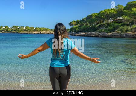 Latina woman, seen from behind, in sportswear, looking at the sea, breathing deeply. Stock Photo