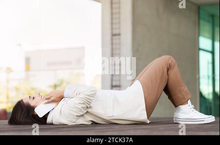 Una giovane donna d'affari europea, allegra e giovane, si trova sulla panchina mentre parla al telefono, all'aperto Foto Stock