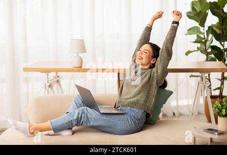 Una giovane donna felice e rilassata che si rilassa a casa, usando un notebook Foto Stock