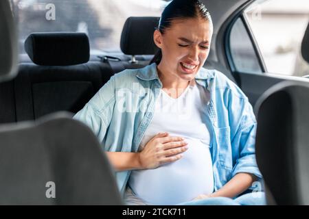 Donna incinta in auto che soffre di dolori di travaglio che stringe l'addome Foto Stock