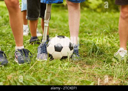 Sezione bassa di ragazzo con gamba amputata che gioca a calcio mentre si trova al parco Foto Stock