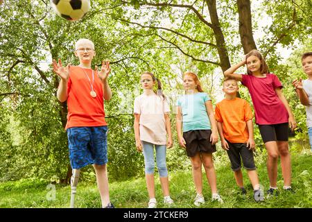 Amici maschi e femmine che guardano un ragazzo disabile che lancia palla da calcio mentre si trova al parco Foto Stock