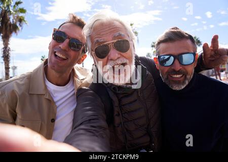 Allegro gruppo di uomini caucasici di mezza età che indossano occhiali da sole che scattano un selfie con un cellulare. Foto Stock