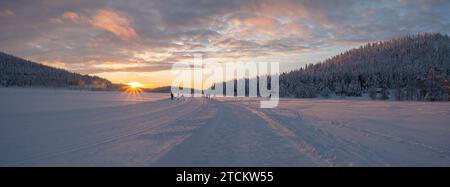 Paesaggio invernale, tramonto sulla foresta innevata e lago ghiacciato in Lapponia. Alberi coperti di neve al sole. Foto panoramica. Foto Stock