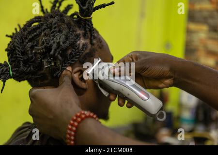 Primo piano della testa di un cliente che riceve un taglio di capelli dal suo barbiere in Africa. Foto Stock