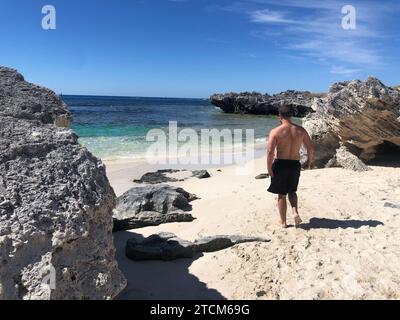 Un giovane si trova su una spiaggia, guardando il vasto oceano Foto Stock