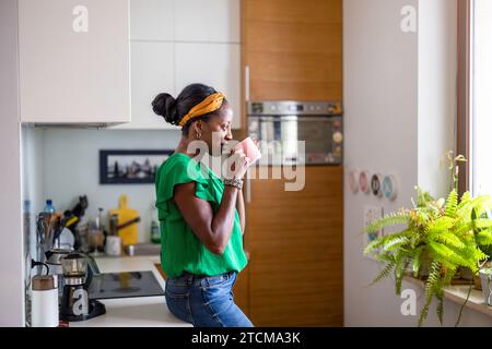 Ritratto di una donna matura sorridente in piedi nella sua cucina che beve caffè Foto Stock