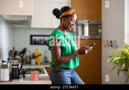 Donna sorridente che usa lo smartphone in cucina a casa Foto Stock