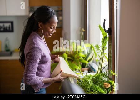 Bella donna che annaffia le piante a casa Foto Stock