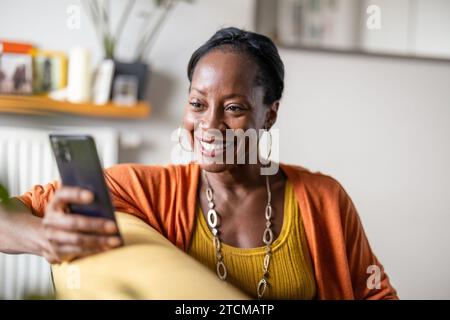 Bella donna che usa il telefono cellulare mentre si rilassa sul divano a casa Foto Stock