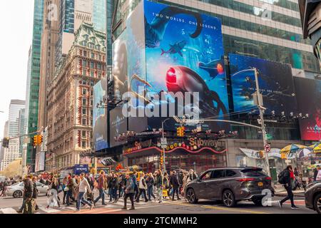 Orde di persone attraversano West 42nd Street sotto la pubblicità per la Warner Bros. Picture'"Aquaman, The Lost Kingdom" film in Times Square a New York sabato 2 dicembre 2023. Il film dovrebbe essere distribuito il 22 dicembre e fa parte dei franchise della DC Comics. (© Richard B. Levine) Foto Stock