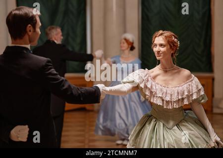 Vista laterale ritratto di una bellissima giovane donna che balla con un partner gentiluomo nella sala da ballo del palazzo Foto Stock