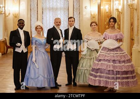 Vista a tutta lunghezza di un gruppo di persone che indossa costumi vittoriani che guardano la macchina fotografica in piedi nella sala del palazzo Foto Stock