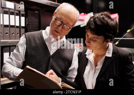 Anziano detective privato che lavora straordinari in un caso penale con un agente di polizia, analizzando le prove della scena del crimine in sala aralveare. Gli investigatori stanno pianificando una strategia per catturare sospetti misteriosi Foto Stock