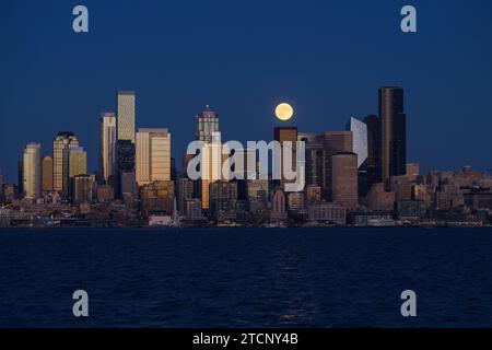 Seattle, WA, USA - 28 ottobre 2023; Hunter's Moon sorge dietro lo skyline del centro di Seattle e Elliott Bay con edifici che brillano al tramonto Foto Stock