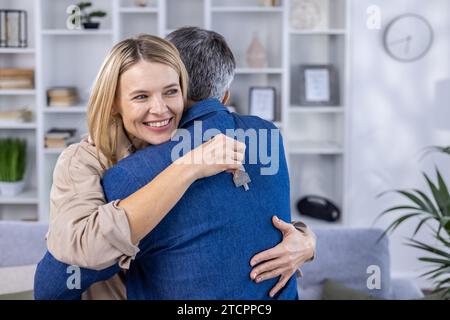 Un marito e una moglie si abbracciano in un nuovo appartamento, la coppia felice è felice con i compratori dell'appartamento. Foto Stock