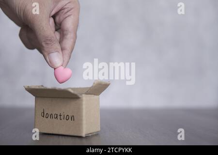 Mano che mette il cuore nella scatola della donazione. Spazio di copia per il testo. Concetto di donazione di organi. Foto Stock