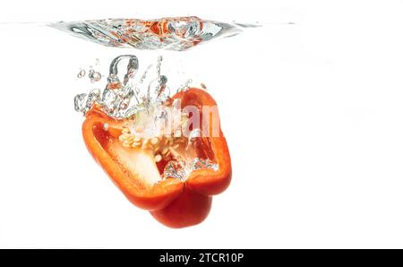 Tagliato a metà peperone rosso cade in acqua, causando bolle e acqua sparsa. Concetto di cibo salutare Foto Stock