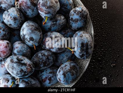 Prugne mature bagnate coperte da gocce d'acqua, primo piano. Un mazzo di frutta di fondo Foto Stock