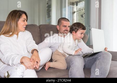 Famiglia che utilizza un computer portatile con un bambino seduto sul divano a casa Foto Stock