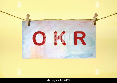 Obiettivi OKR, lettere chiave e risultati su carta colorata appesa di fronte a uno sfondo giallo con una corda e un clothespins Foto Stock