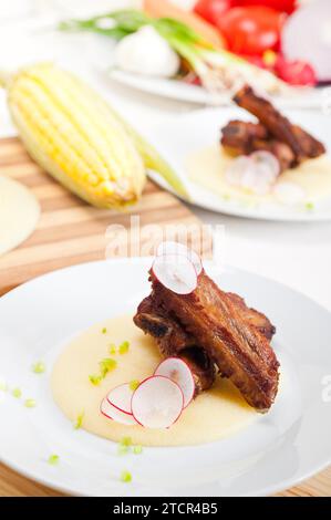 Costolette di maiale arrosto italiane tradizionali servite su un letto di polenta e crema di mais Foto Stock