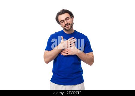 giovane bruna europea con la barba in una maglietta blu ha chiuso gli occhi su uno sfondo bianco con spazio per le copie Foto Stock