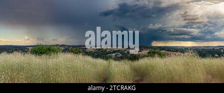 Una vista panoramica su una collina erbosa con nuvole scure che cadono in lontananza dalla pioggia intensa a Guildford, nel Victoria centrale, Australia. Foto Stock