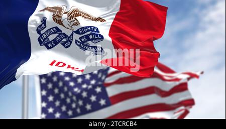 Primo piano della bandiera dello stato dell'Iowa che sventola al vento con la bandiera nazionale americana in una giornata limpida. rendering dell'illustrazione 3d. Tessuto ondulato. Messa a fuoco selettiva Foto Stock