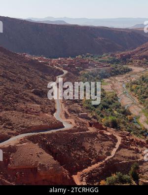 Vista sopraelevata su una strada tortuosa e tradizionale villaggio in terra vicino a un fiume nelle montagne dell'Atlante ad est di Marrakech, Marocco, 13 dicembre 2023 Foto Stock