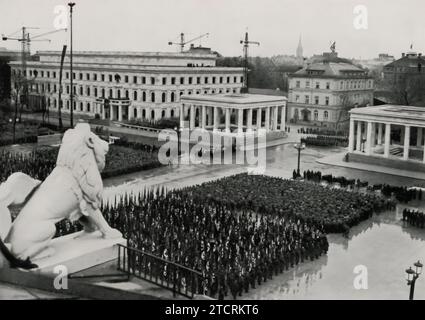Il 9 novembre 1935, le formazioni del Partito Nazionalsocialista sono riunite sul quasi completato Königsplatz. Questa immagine cattura Adolf Hitler supervisionando l'evento, in piedi nella sua auto a tetto aperto e salutando. La data, significativa per commemorare il Putsch della Beer Hall, e il luogo, Königsplatz, un luogo chiave per i raduni nazisti, sottolineano l'importanza di questo giorno nel calendario nazista. La presenza di Hitler e le formazioni meticolosamente organizzate riflettono l'enfasi del regime sulla disciplina, l'ordine e il potere simbolico degli incontri di massa. Foto Stock