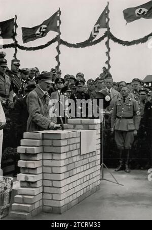 Adolf Hitler è visto mentre posa la prima pietra per la sala delle assemblee di Adolf Hitler Koog, un evento significativo che segna lo sviluppo di questa zona. Adolf Hitler Koog, parte dei progetti di bonifica e insediamento del regime, prese il nome da Hitler, simboleggiando gli sforzi nazisti nello sviluppo agrario e rurale. La cerimonia di posa della prima pietra, tipicamente un atto importante e simbolico, sottolinea l'importanza che il regime ha posto su tali progetti di costruzione, riflettendo la sua attenzione sulla rimodellatura e la coltivazione della terra come parte dei suoi più ampi obiettivi ideologici. Foto Stock