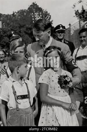 Adolf Hitler è spesso raffigurato circondato da bambini, un tema ricorrente nella propaganda nazista, come si vede in questa immagine dove è accompagnato da Baldur von Schirach, il leader della Gioventù Hitler, a destra. Queste interazioni in scena furono progettate per ritrarre Hitler come una figura paterna e accessibile, rafforzando la sua immagine pubblica. La presenza di von Schirach sottolinea l'enfasi del regime sull'indottrinamento dei giovani con l'ideologia nazista, con l'obiettivo di plasmare le credenze e la lealtà della prossima generazione. Foto Stock