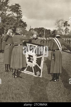 Le reclute tedesche vengono catturate prendendo il Führereid (giuramento di Hitler) alla bandiera tedesca durante il loro addestramento militare. Questa solenne cerimonia segna un momento significativo nella loro iniziazione, simboleggiando il loro impegno e la loro lealtà al regime. L'atto di giurare fedeltà alla bandiera, un potente simbolo nazionale, riflette l'indottrinamento e l'intenso senso di dovere infuso nei soldati come parte della loro indottrinazione militare durante questo periodo della storia. Foto Stock